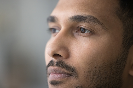 Thoughtful handsome young Indian man facial close up portrait. Face of pensive serious attractive guy with stylish stubble, beard, looking away, thinking, dreaming