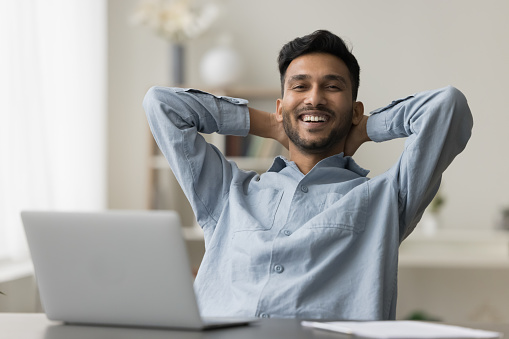 Portrait of happy successful young business man enjoying leisure, relaxing in work armchair, smiling at camera, laughing, stretching body, celebrating success, achievement