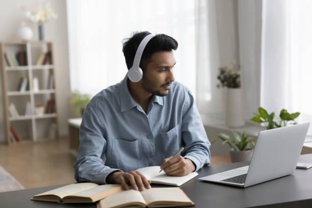 Focused Indian student in wireless headphones watching online educating seminar