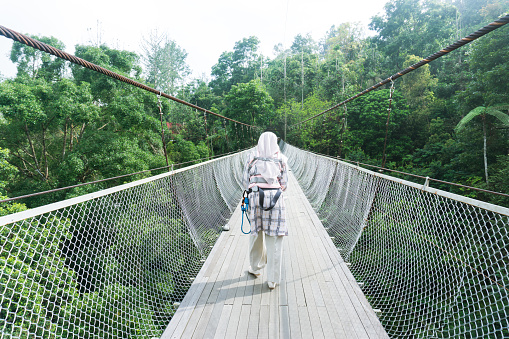Rear view of mother and her baby walking on the suspension bridge carefully, using a safety belt procedure and cradling her baby in front