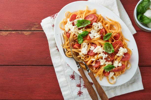 salat-caprese oder pasta-spaghetti gebrochen mit basilikum und mozzarella ala caprese auf einem weißen teller auf rotem rustikalem holzhintergrund. traditionelle italienische küche. italienisches food-konzept.  draufsicht. - caprese salad antipasto wine mozzarella stock-fotos und bilder