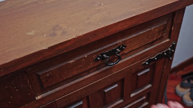 A man's hand opens the drawer of an old chest of drawers, puts the document inside.