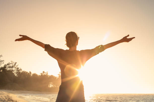 La giovane donna si crogiola nei caldi raggi di sole al tramonto con le braccia distese. - foto stock