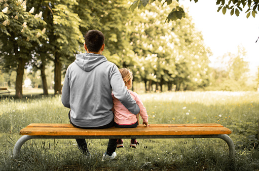 Father and his daughter sitting on the bench in the park.