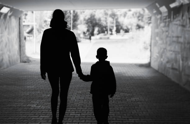 Siluetta del bambino della madre che cammina in un ambiente urbano di strada - foto stock