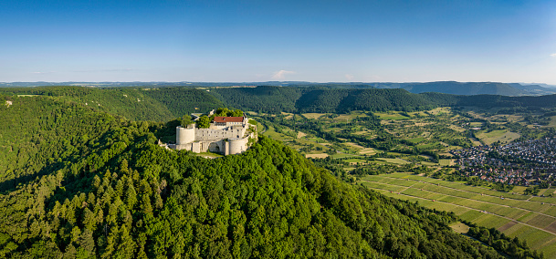 Neuffen, Germany - June 11, 2023: Burg Hohenneuffen - Hohenneuffen Castle on Hill Top of Swabian Alb in Summer. Aerial Drone view over the green summer Swabian Alb Hill Range and Burg Hohenneuffen - Hohenneuffen Castle under blue cloudless summer sky. Illuminated from warm sunset light.  Stitched XXXL Panorama from Mavic 3 Pro Drone. Neuffen, Hohenneuffen Castle, Esslingen, Swabian Alb, Baden Württemberg, Southern Germany, Germany, Europe.