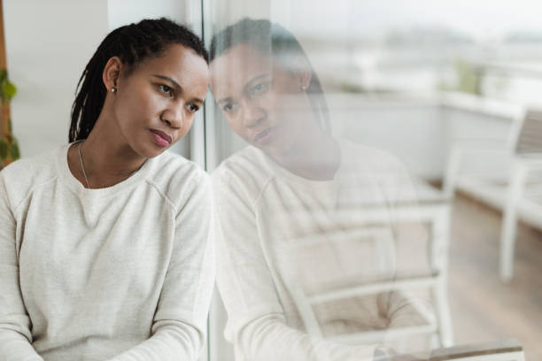 Pensive black woman looking through window from home.