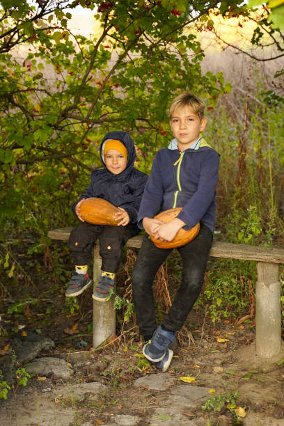 istock Children sit on a bench with pumpkins, preparing for Halloween. 1501790366