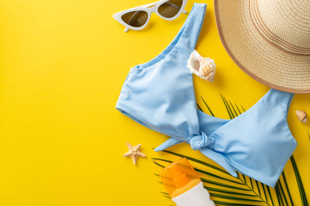 istock Safe sunbathing concept. Top view arrangement featuring sunscreen bottle, stylish sunglasses, sunhat, blue bodice, seashells, starfish, palm leaf on vivid yellow backdrop with space for advertisement 1501792790