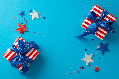Expressive congratulations for Independence Day USA. Top view perspective highlighting glimmering stars, confetti, thematic gift boxes wrapped beautifully on blue backdrop featuring space for greeting
