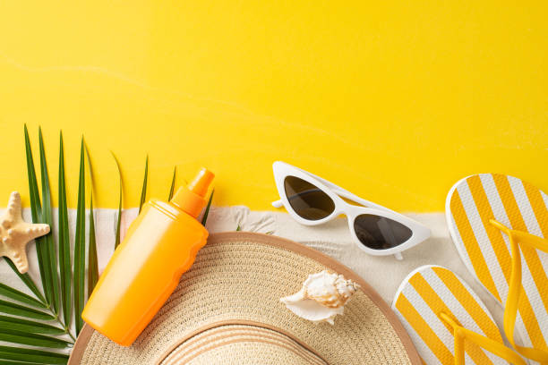 istock Summer Sun Essentials: Top view visual feast for UV Awareness Month, featuring top-view SPF cream bottle, sunglasses, hat, flip-flops, shell, starfish, and palm leaf on vivid yellow and sandy canvas 1501794166
