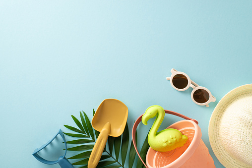 Tropical resort with kids. Top view photo of empty space with palm leaves and shells, sand toys, sunglasses and panama hat on blue isolated background with copyspace