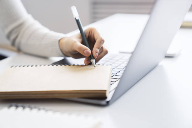 istock The image focuses on a woman's hand scribbling in a notepad on a stylish laptop, set against a blurry scene 1501805124