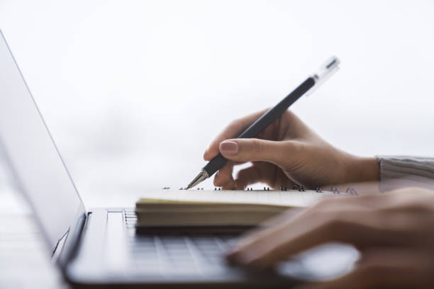 istock In close view, a woman's hand writing down notes in a notepad on a laptop, against a hazy backdrop 1501806075