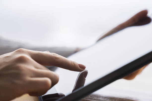 istock Woman's finger touching a sleek digital tablet screen placed on a desk, within the softly lit blur of an active office environment 1501806076