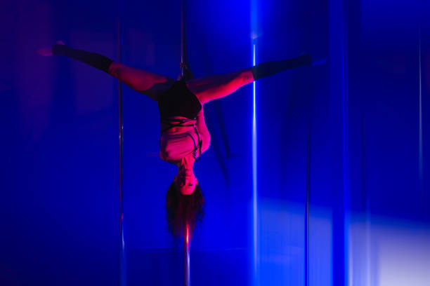 istock Girl dancer in gymnastic splits on a pole upside down on a blue background. 1501808346