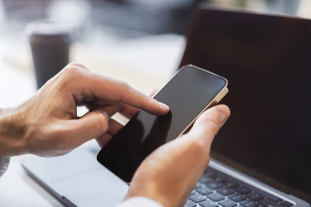 istock Focused image of a woman navigating her high-tech smartphone, laptop open next to her amidst the blur of a busy office setting 1501809354