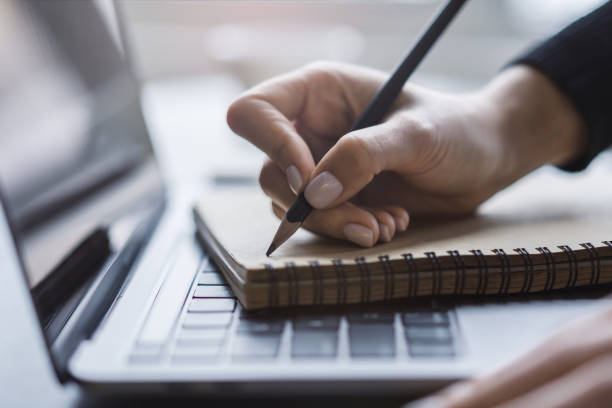 istock Detailed view of a woman's hand taking notes in a notepad on a cutting-edge laptop, against a blurred backdrop 1501811587