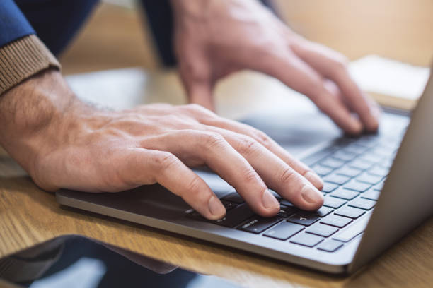 Set against a blurry office backdrop, the image captures a man's hands in close detail, typing on a cutting-edge laptop keyboard