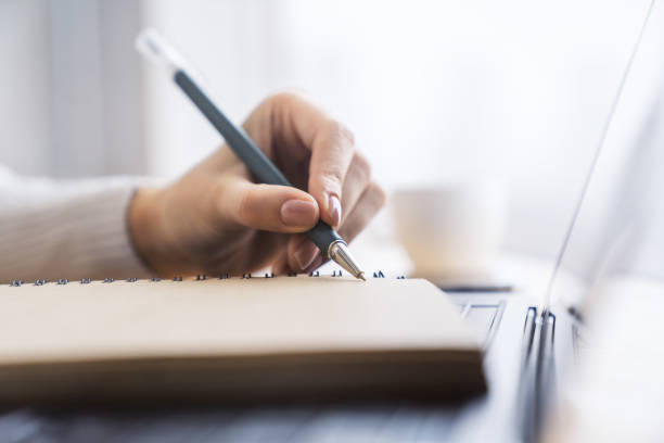istock A woman's hand seen in close-up, writing in a notepad, against a soft-focus backdrop 1501818899