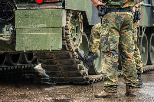 Dos soldados con uniforme de camuflaje de pie durante un descanso bajo la lluvia cerca de las orugas de un tanque blindado photo