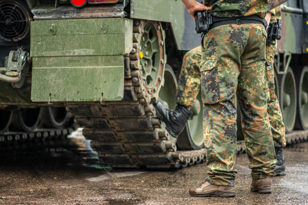 dos soldados con uniforme de camuflaje de pie durante un descanso bajo la lluvia cerca de las orugas de un tanque blindado - defense industry fotografías e imágenes de stock