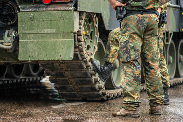 Two soldiers in camouflage uniform standing during a break under the rain near the tracks of an armoured tank Two soldiers in camouflage uniform standing during a break under the rain near the tracks of an armoured tank, only the trousers and the boots are visible militant groups stock pictures, royalty-free photos & images