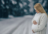 Pregnant woman looking down her belly at snowy forest