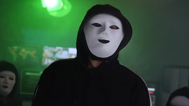 Three masked hackers sit in a darkroom. Computer criminals in secret subway location.
