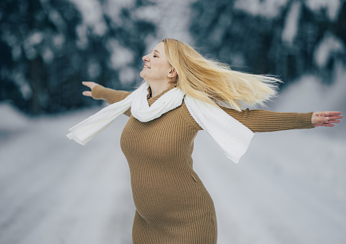 Cheerful pregnant woman spending leisure time at snowy landscape with her arms outstretched