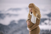 Pregnant woman looking down her belly at snowy forest