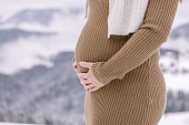 Woman in warm clothing touching her pregnant belly