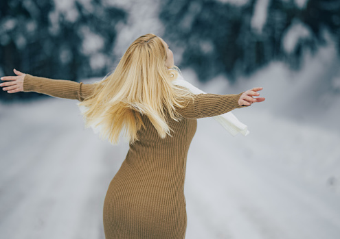Carefree woman in warm clothing spending leisure time at snow covered landscape with her arms outstretched