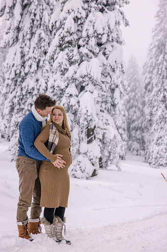 Loving husband embracing from behind and touching pregnant belly of his wife on snow covered landscape