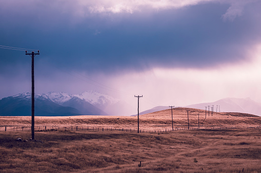 Photograph of telephone poles running through a valley against snow capped mountains on the South Island of New Zealand