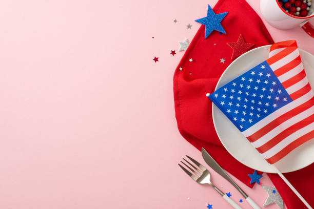Independence Day party essentials: Top view of table decoration including plate, cutlery, cup, napkin, shiny stars, confetti, and national flag. Pastel pink background with space for text or ad os esenciales de la fiesta del día de la independencia: vista superior de la decoración de la mesa, incluido el plato, los cubiertos, la taza, la servilleta, las estrellas brillantes, el confeti y la bandera nacional. fondo rosa pastel con espacio