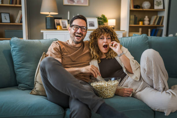 Couple caucasian man and woman sit at home on sofa bed watch tv movie stock photo