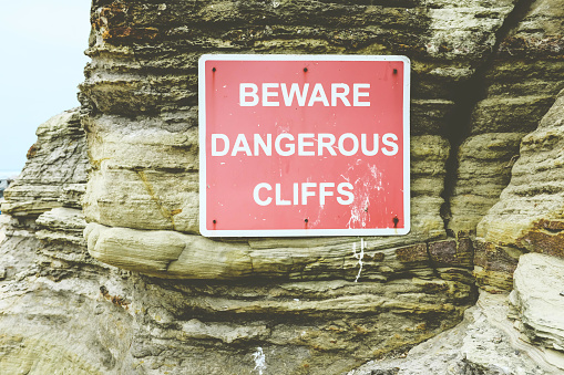 Danger falling rocks sign on side of cliff