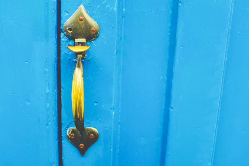 A well worn old brass golden door handle on a bright blue wooden door