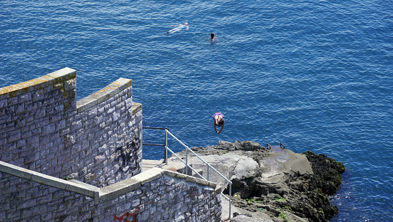 Plymouth, Devon, England - July 6 2022: People spending leisure time at Plymouth Sound bathing in the cool blue sea and walking along the harbour walls