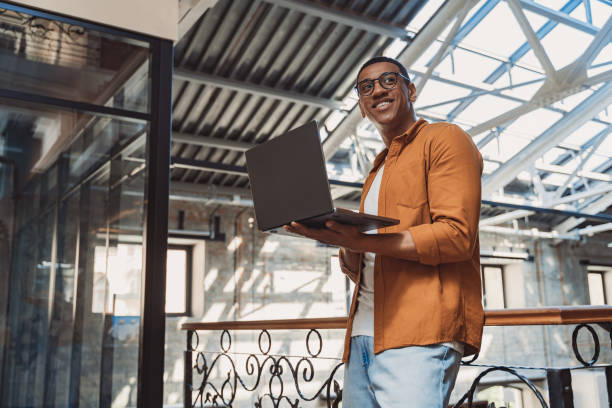 Smiling businessman in casual clothing working on laptop while standing on coworking background stock photo