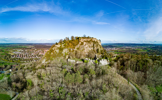 Panorama of a high green wooded hill with the ruins of the ancient historical Hohentwil castle on its top, against a bright blue sky in the sunlight