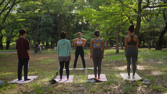 A group of multi-ethnic people are taking part in a yoga class in nature. A Black ethnic female yoga instructor is teaching yoga to a group of multi-ethnic people in nature.