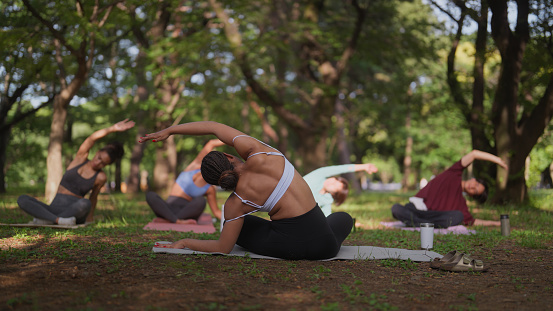 A group of multi-ethnic people are taking part in a yoga class in nature. A Black ethnic female yoga instructor is teaching yoga to a group of multi-ethnic people in nature.