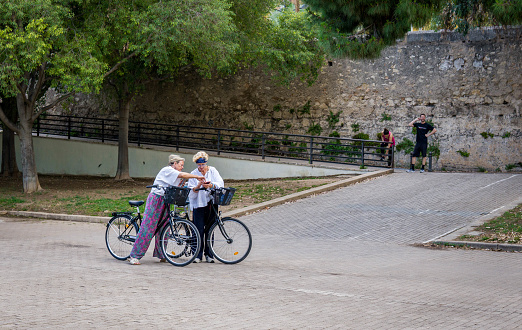 Picture of Two Elderly Tourists on Bicycles Seeking Orientation with their Mobile Phone in the Middle of a Park Visiting the City