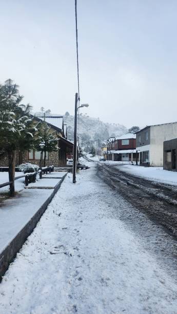 Calle de Caviahue, city of Neuquen, with a snow-covered dirt street, houses on the sides and a light column, with a mountain with snow-capped trees behind stock photo