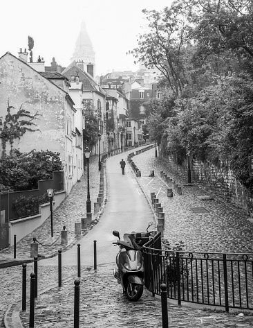 Paris, France, November 10, 2016: A man walks up the hill in Montmartre on a foggy day in Paris. A motorcycle sits at the bottom of the hill.