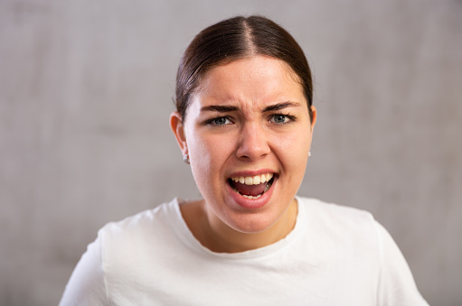 Close-up portrait of young woman with angry expression on face against light unicoloured background