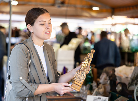 Smiling female tourist checking out handcrafted wooden statuette at flea market