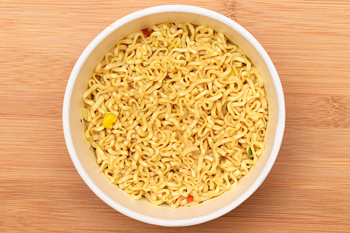 Instant Noodles in Disposable Cup on Wooden Background - Top View. Asian Fast Food. Quick Lunch